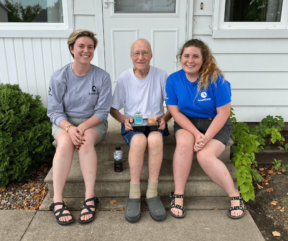 Photo of Meals on Wheels volunteers sitting with a client outside their home.